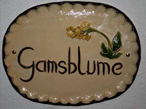 A decorative sign with the text "Gamsblume" and a small floral design. - Ferienwohnung Gamsblume, 2 Personen, 54 m², Dusche/WC, Flat-TV, 1 Schlafzimmer, Balkon, Infrarot-Wärmekabine, Nichtrauche (Ramsau bei Berchtesgaden)