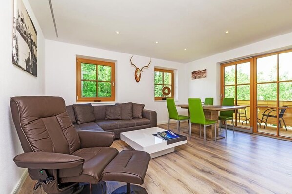 A modern living room with a sectional sofa, a coffee table, and a dining area with green chairs.