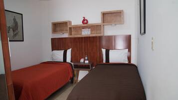 Habitación de hotel con dos camas individuales, cabeceros de madera, una mesita con una botella de agua y un cuadro enmarcado en la pared.