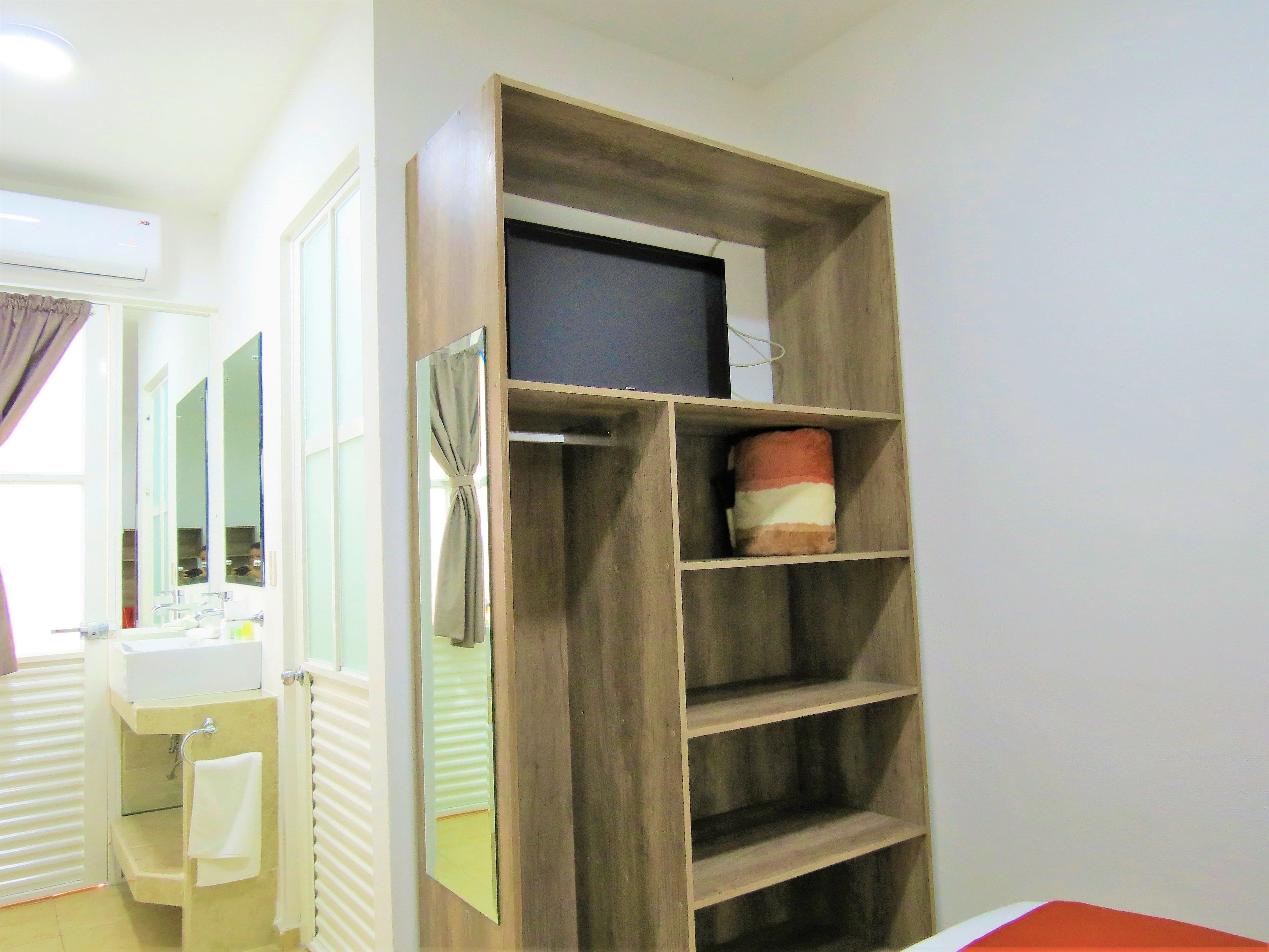 A bathroom with a vanity, mirror, and a wooden shelf unit with a television.