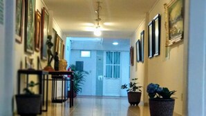 Un couloir avec un ventilateur de plafond, des tableaux encadrés accrochés aux murs et des plantes en pot.