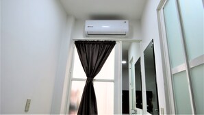 Une pièce dotée d’un climatiseur fixé au plafond, d’une fenêtre avec un rideau et d’un miroir qui reflète une partie de la pièce.