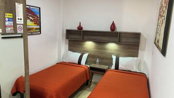 Een hotelkamer met twee bedden, elk met een oranje sprei, een houten hoofdbord en een klein tafeltje met een waterfles. Op het hoofdbord staan twee rode vazen.