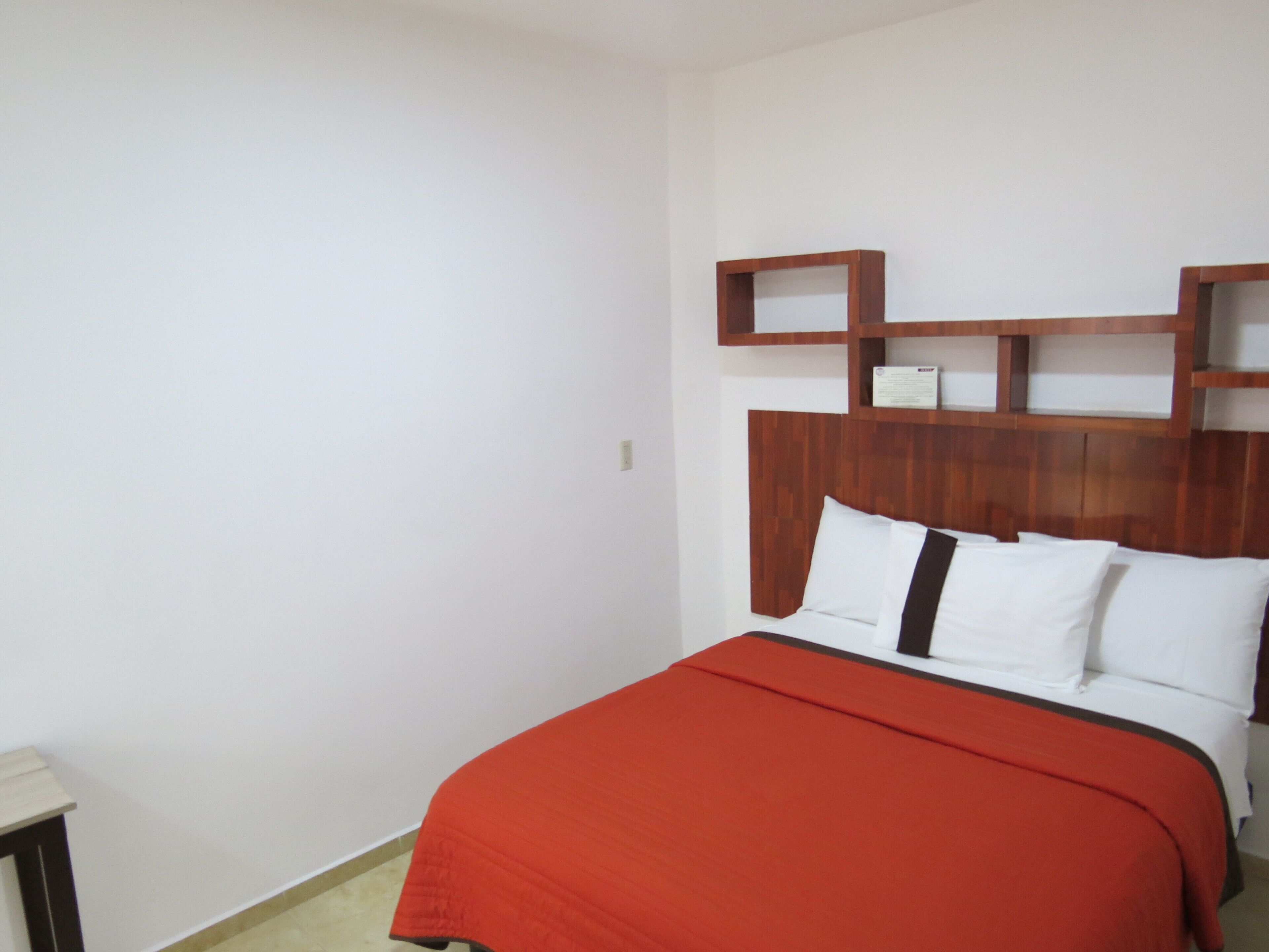 Un dormitorio con cabecera de madera, colcha roja y ropa de cama blanca.