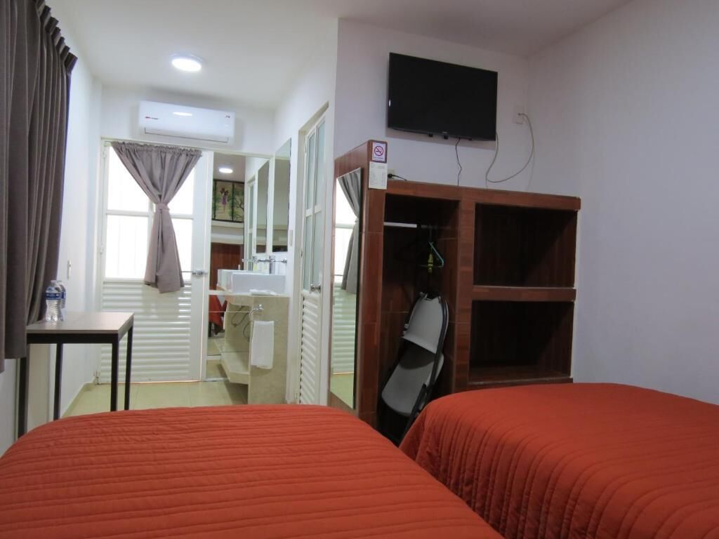 Une chambre d’hôtel avec deux lits, une télévision, un appareil de climatisation, un porte-manteau et une salle de bain visible à travers une porte ouverte.