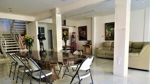 Un vaste espace de salle à manger avec une table en marbre et des chaises modernes, un escalier et un coin salon comprenant un canapé et des œuvres d’art.