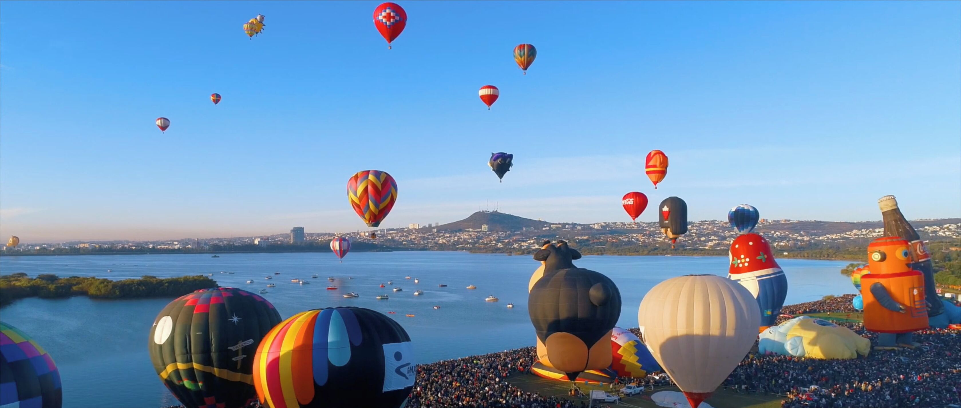 Una gran multitud se reunió junto a la orilla del agua, con numerosos globos aerostáticos en el cielo.