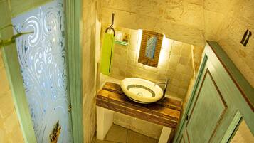 A bathroom with a stone wall, a wooden vanity, a sink, and a mirror.
