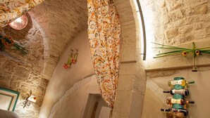 A stone-walled room with a patterned curtain, a wall-mounted wine rack, and a rustic chandelier. - Relais Santa Maria (Martina Franca)
