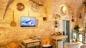A rustic stone-walled room with a television, wicker furniture, a small table, and a door leading to another room. - Relais Santa Maria (Martina Franca)