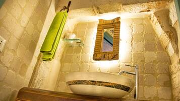 Une salle de bain avec un mur en pierre, un miroir encadré en bois, un lavabo blanc et une serviette verte accrochée à un crochet.