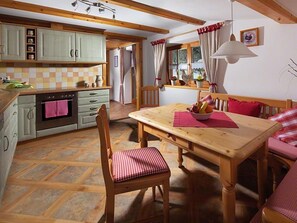 A kitchen with wooden cabinets, a dining table with chairs, and a window with curtains. - Ferienwohnung Lärcheck für 2-6 Personen (Marktschellenberg)