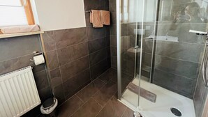 A modern bathroom with a glass shower enclosure, dark tiled walls, and a white radiator.
