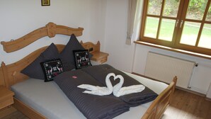 A wooden bed with grey bedding, two decorative pillows, and a swan-shaped towel arrangement.