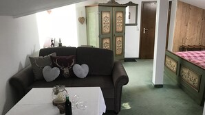 A cozy room with a sofa, a table with a bottle and glasses, a cabinet with decorative panels, and a bed with a checkered bedspread. - Apartment 3, 25sqm, balcony, living/bedroom, kitchen, WLAN, FLat-TV (Ruhpolding)