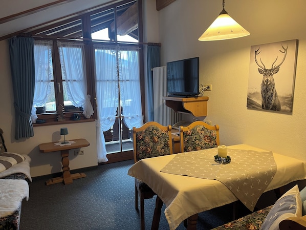 Une pièce chaleureuse avec une table à manger, des chaises, un téléviseur et un tableau représentant un cerf.