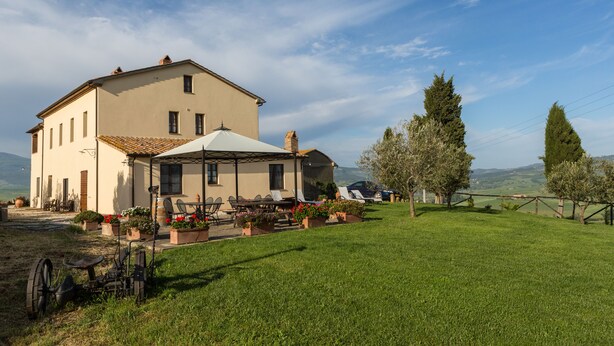 A large, single-story building with a tiled roof, a covered patio area with outdoor seating, and a well-maintained lawn. - Agriturismo Poggio Tobruk (Pienza)