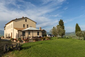 A large, single-story building with a tiled roof, a covered patio area with outdoor seating, and a well-maintained lawn. - Agriturismo Poggio Tobruk (Pienza)