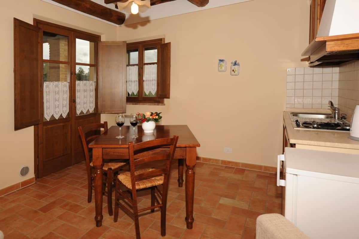 Una cocina con una mesa de comedor, sillas, un refrigerador y un ventanal con cortinas.