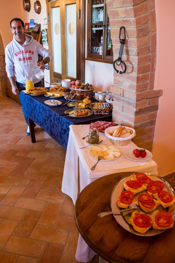 A breakfast buffet with various dishes and a person serving. - Agriturismo Poggio Tobruk (Pienza)