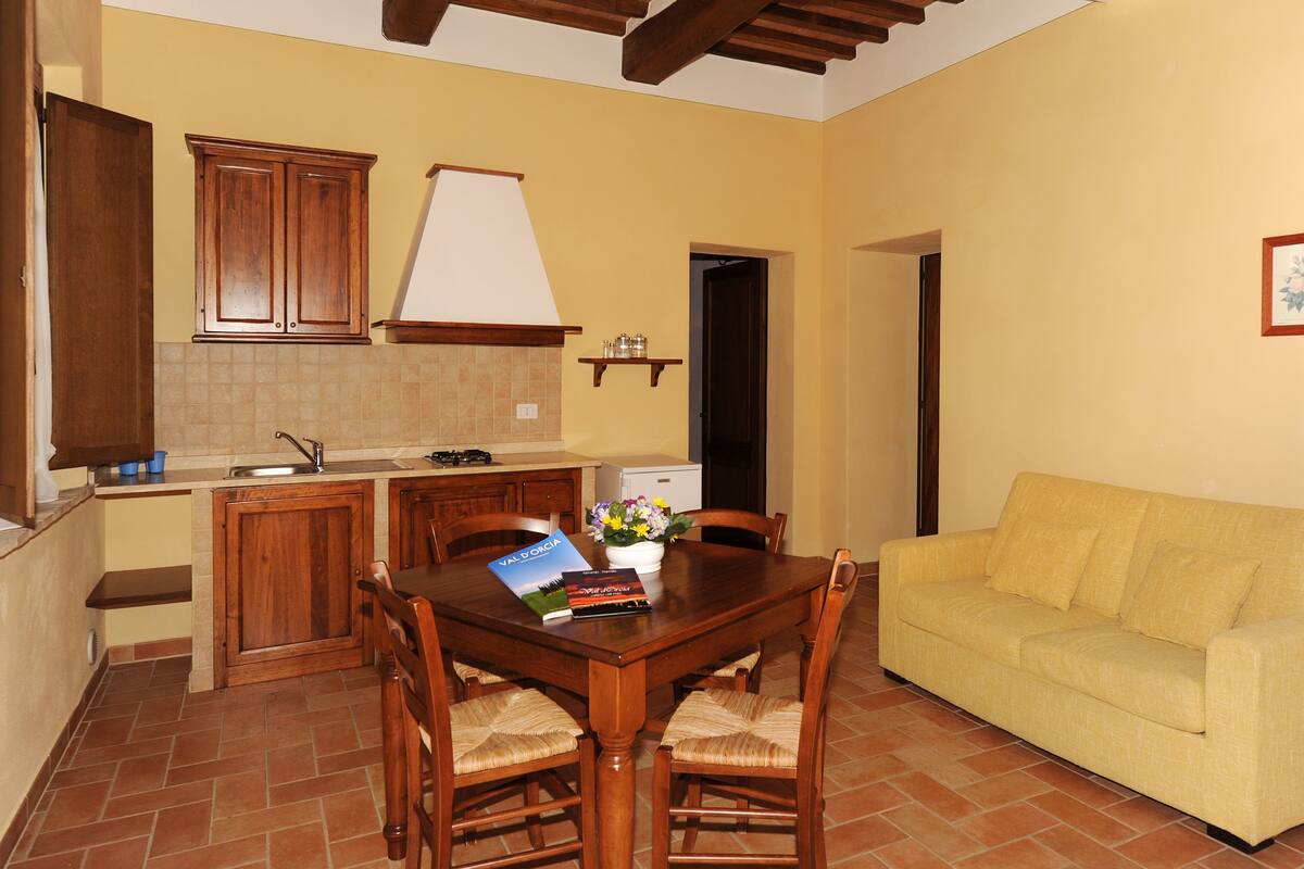 Una cocina compacta con armarios de madera, una mesa de comedor con sillas y un sofá amarillo.