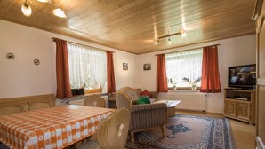 Una habitación acogedora con techo de madera, una mesa de comedor con mantel a cuadros, un sofá y un televisor.