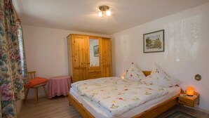 Un dormitorio con cama de madera, una mesita pequeña, una silla, un armario y una mesita de noche con lámpara.