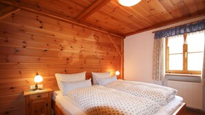 Un dormitorio con paneles de madera, una cama doble, dos lámparas de noche, un ventanal con cortinas y un radiador.