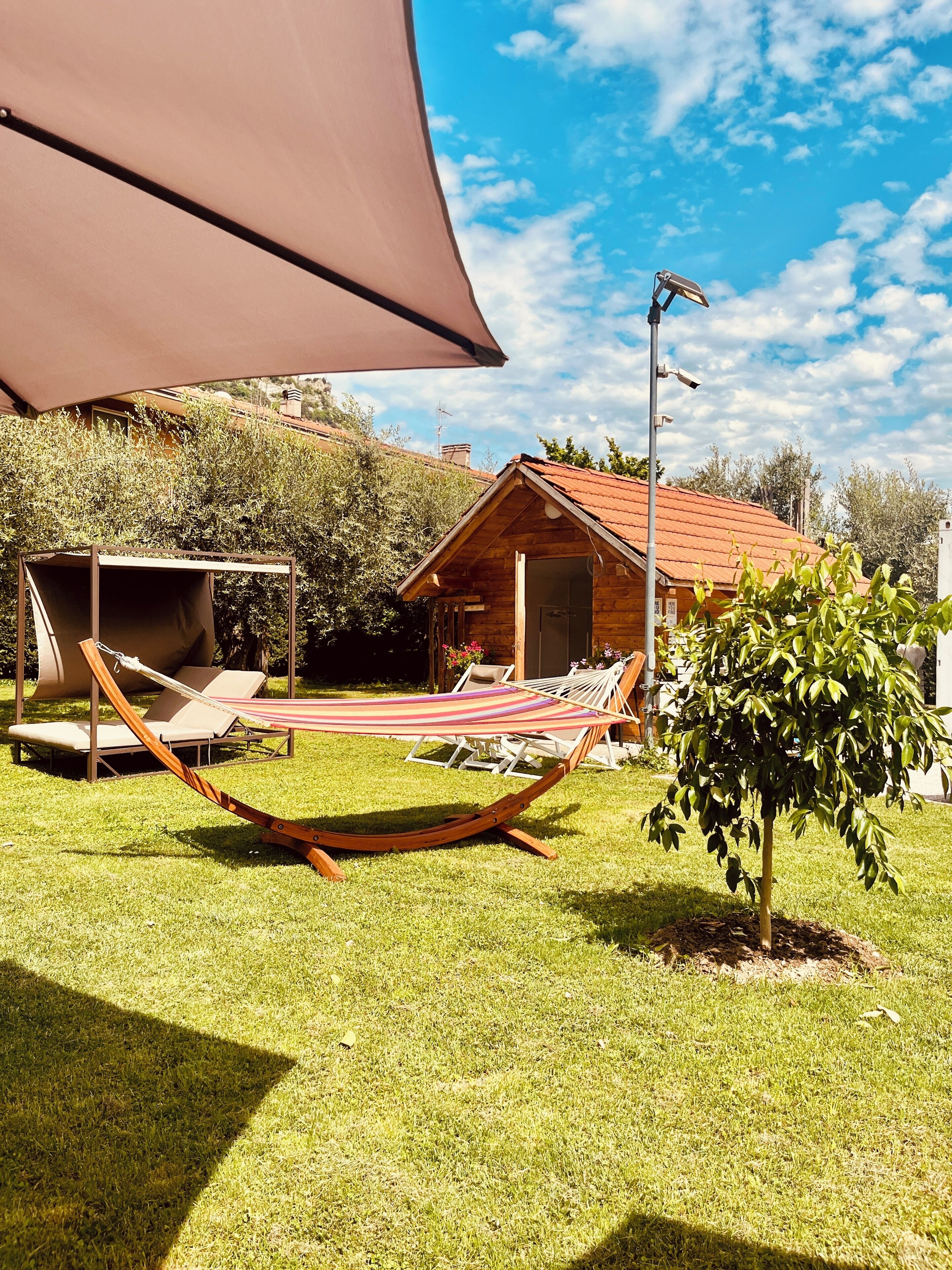 A wooden cabin with a red roof, a hammock, and a small tree in a grassy yard.