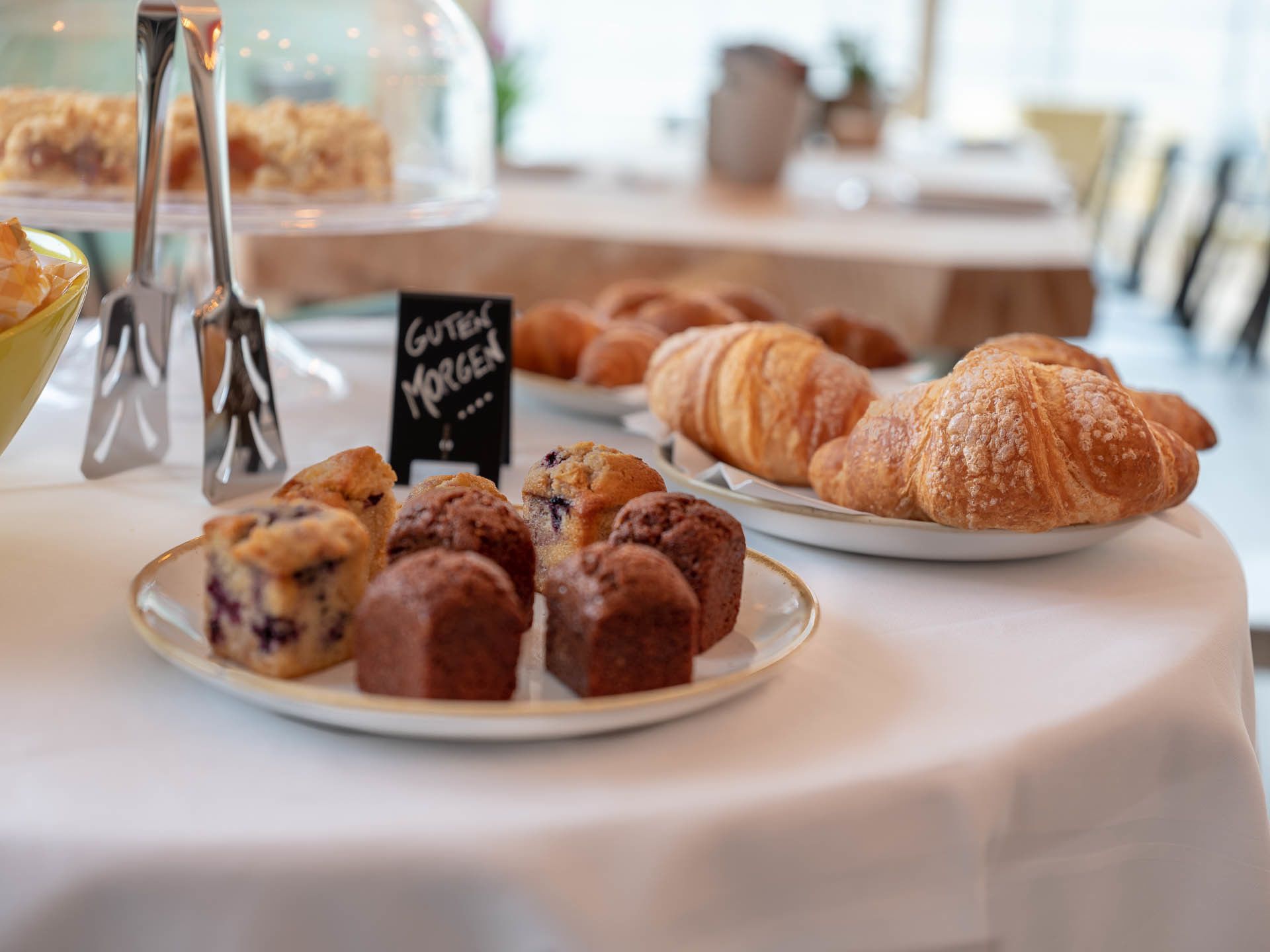 Una mesa de buffet con diversas opciones de panadería, incluyendo muffins y cruasanes.