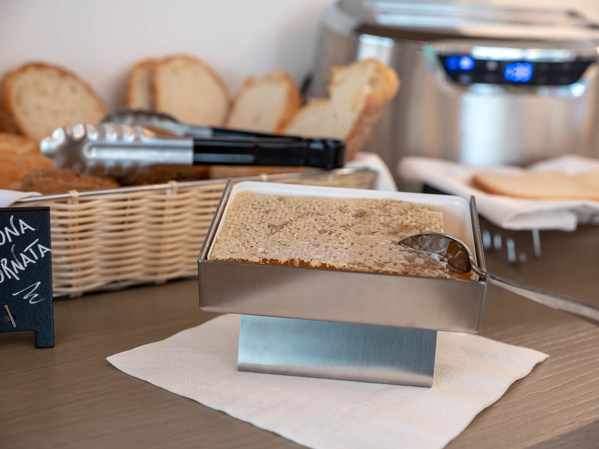 A buffet setup with a bread station, a sign, and a stainless steel appliance in the background.