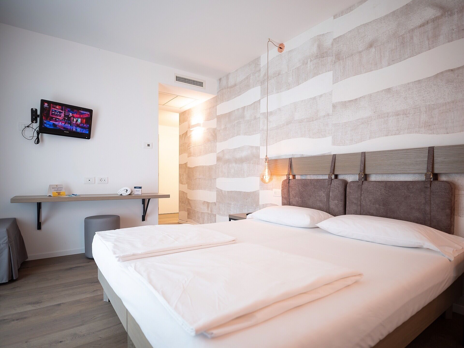 Habitación de hotel moderna con una cama grande, un escritorio con televisor de pantalla plana y una pared con textura original.