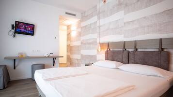 Habitación de hotel moderna con una cama grande, un escritorio con televisor de pantalla plana y una pared con textura original.