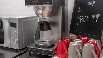 Eine Kaffeemaschine mit digitaler Anzeige, eine Kaffeekanne und ein Schild mit dem Angebot von kostenlosem Kaffee.
