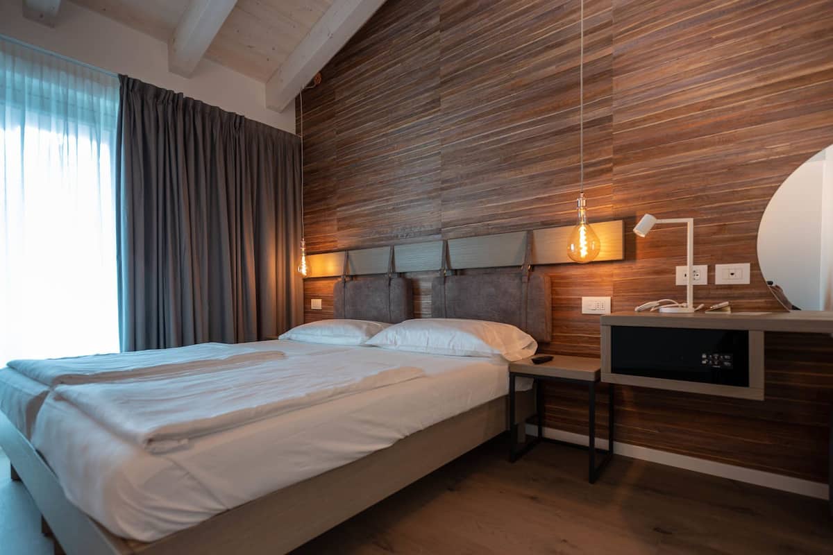 A modern bedroom with a wooden headboard, a bedside table with a lamp, and a built-in TV.