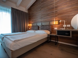 A modern bedroom with a wooden headboard, a bedside table with a lamp, and a built-in TV. - Glocal Torbole (Nago-Torbole)