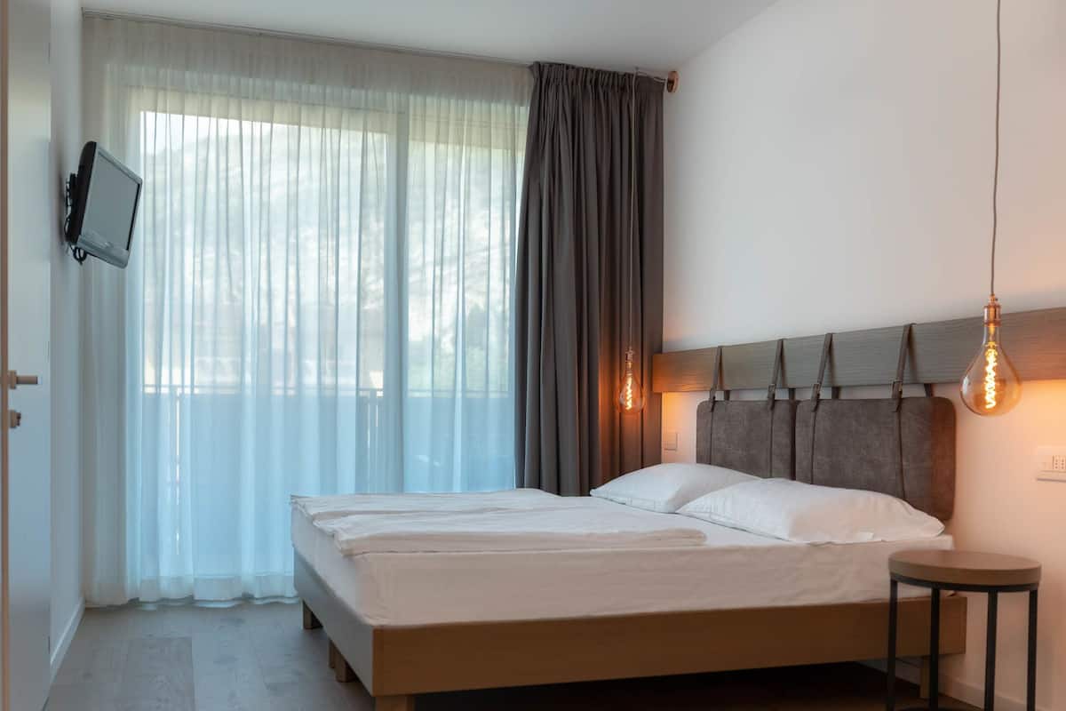 A bedroom with a bed, a television on the wall, and a small table.