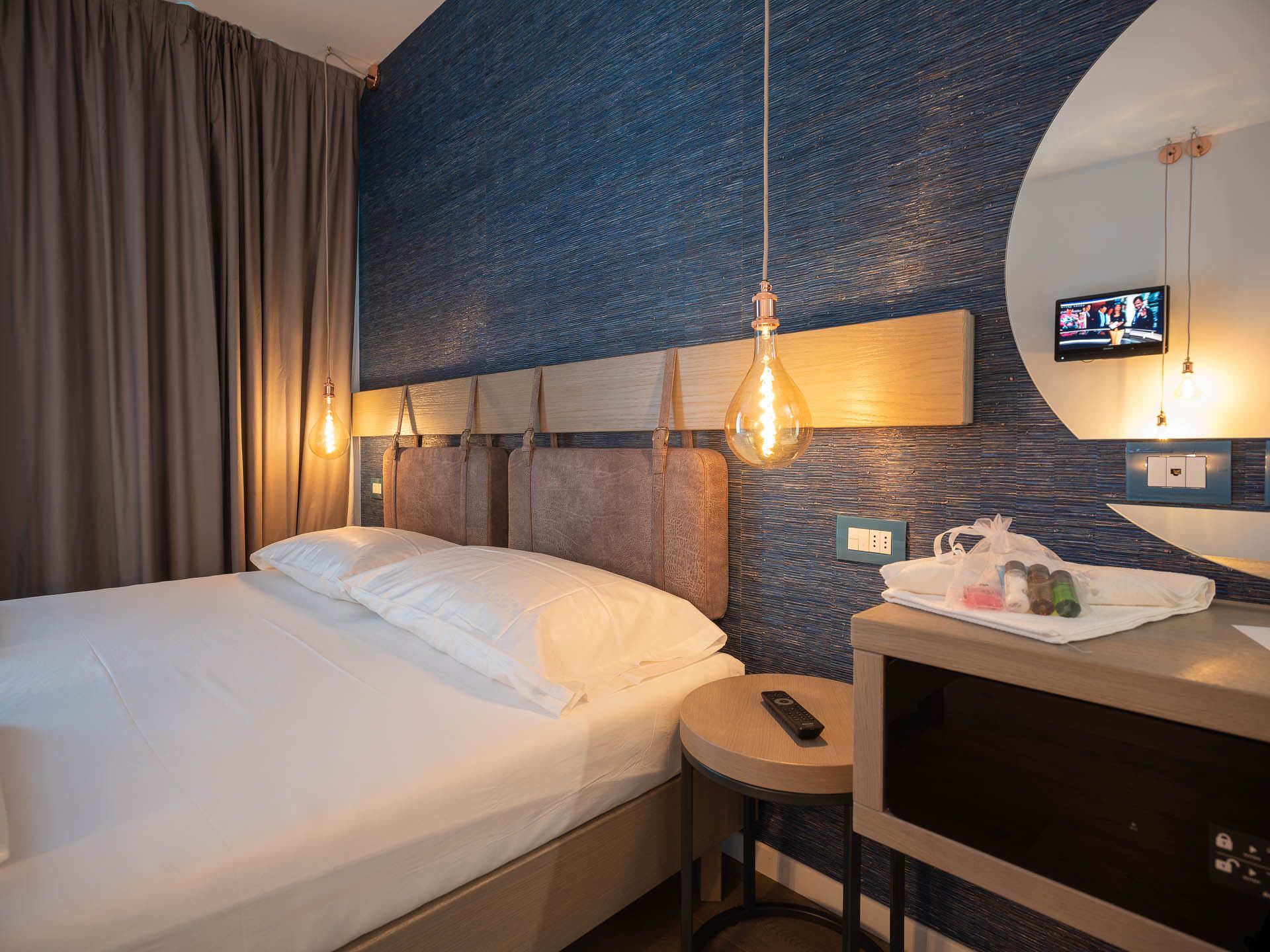 Et hotelværelse med en seng, et rundt bord, et fjernsyn og et vægmonteret fjernsyn.