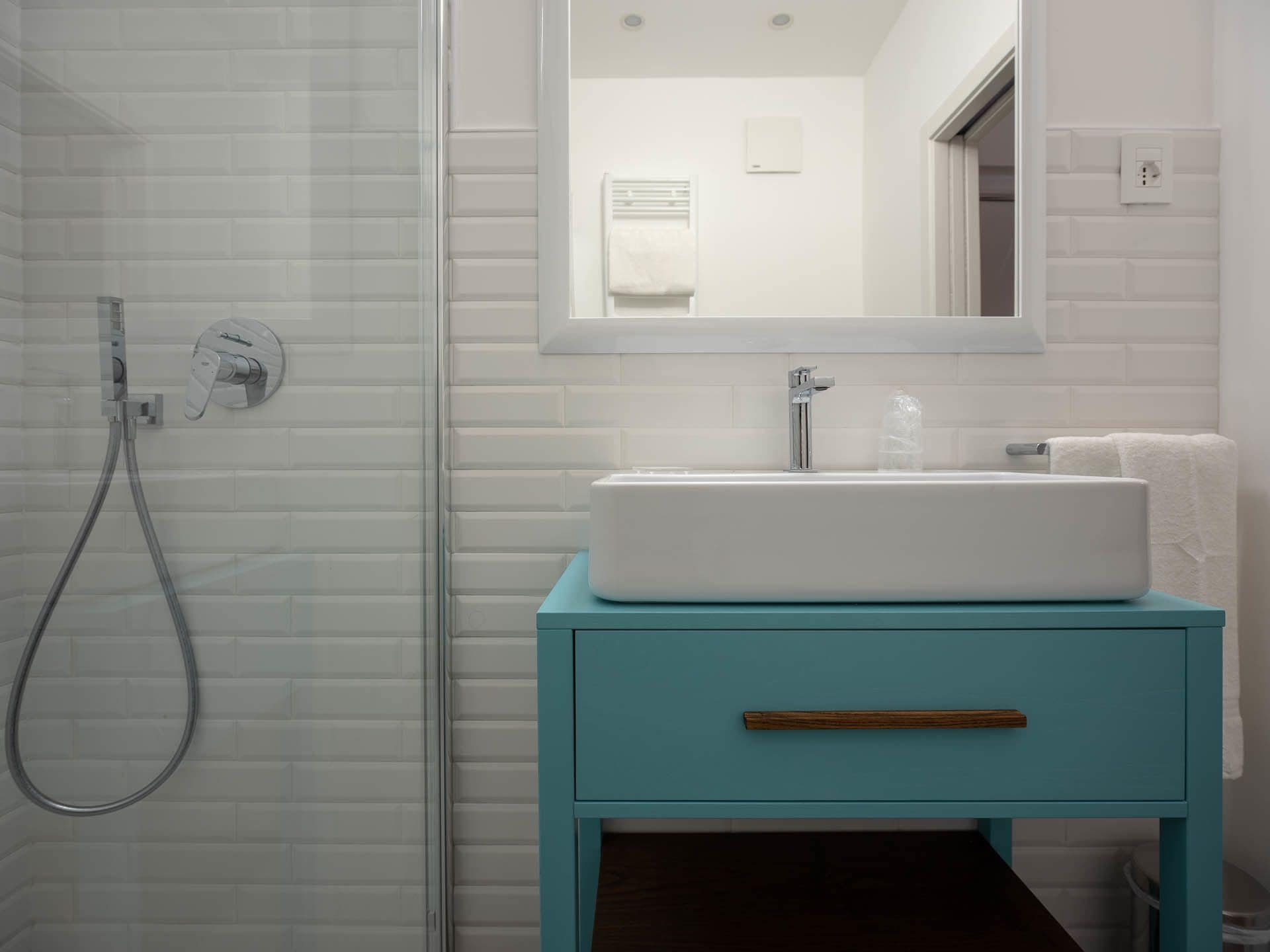 Un baño con cabina de ducha de vidrio, un lavabo blanco y un mueble de tocador verde azulado con cajón de madera.