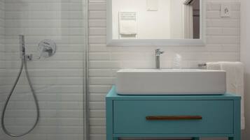 Un baño con cabina de ducha de vidrio, un lavabo blanco y un mueble de tocador verde azulado con cajón de madera.