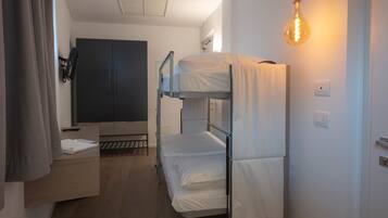 A dormitory room with bunk beds, a wardrobe, a desk, and a hanging light bulb.