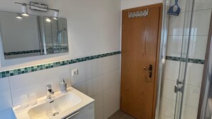A modern bathroom with a white sink, mirror, and glass shower enclosure.