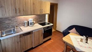 A compact kitchen with wooden cabinets, a built-in oven, and a sink. There's a dining area with a table and chairs.