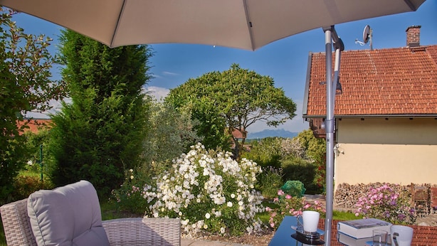 A patio area with a wicker chair and table, a large umbrella, and a view of a house and trees. - Ferienwohnung Nr. 1 - "Panoramablick", 108 qm Obergeschoss, 1 separates Schlafzimmer (Bad Endorf)