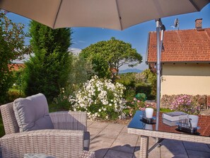 A patio area with a wicker chair and table, a large umbrella, and a view of a house and trees.