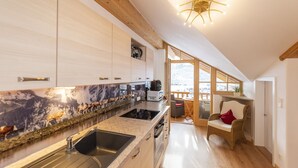 Eine moderne Küche mit Holzschränken, einer Granit Arbeitsplatte und einem eingebauten Herd. Ein Fenster bietet Blick auf Berge, und ein Stuhl ist mit einem roten Kissen ausgestattet.