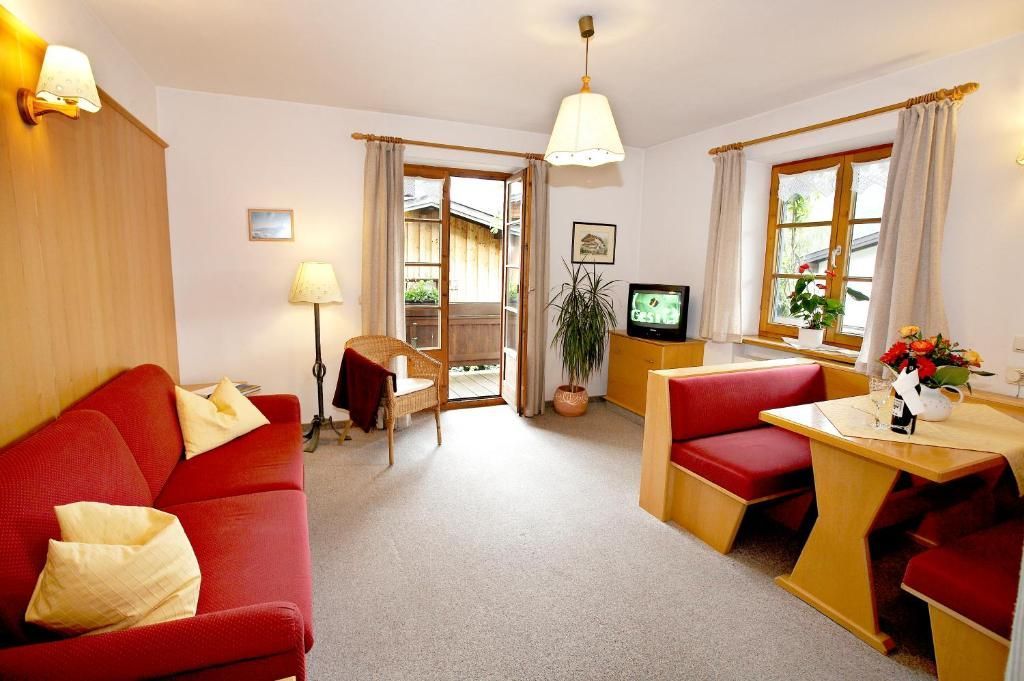 Ein gemütliches Wohnzimmer mit einem roten Sofa, einem Holzesstisch mit roten Bänken, einem Fernseher und einer Topfpflanze.