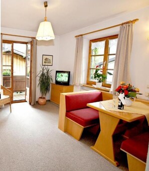 A living room with a red sofa, a wooden dining table with red chairs, a TV, and a balcony.