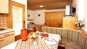 A cozy room with a wooden ceiling, a dining table set with a plaid tablecloth, a sofa, and a television on a wooden cabinet.