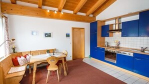Una cocina acogedora con vigas de madera, una zona de comedor con banco y armarios azules.